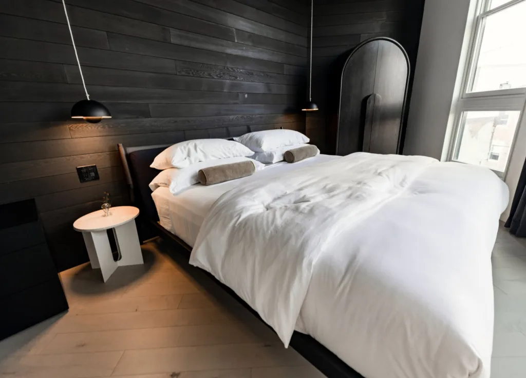 Opgemaakt bed met een dik wit dekbed in een slaapkamer met een donkere houten wand